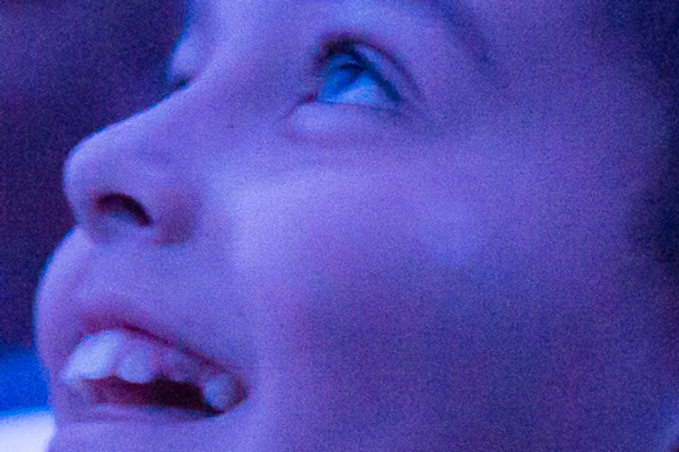 People seated in a theater, smiling and pointing towards the screen. The lighting creates a blue ambiance.