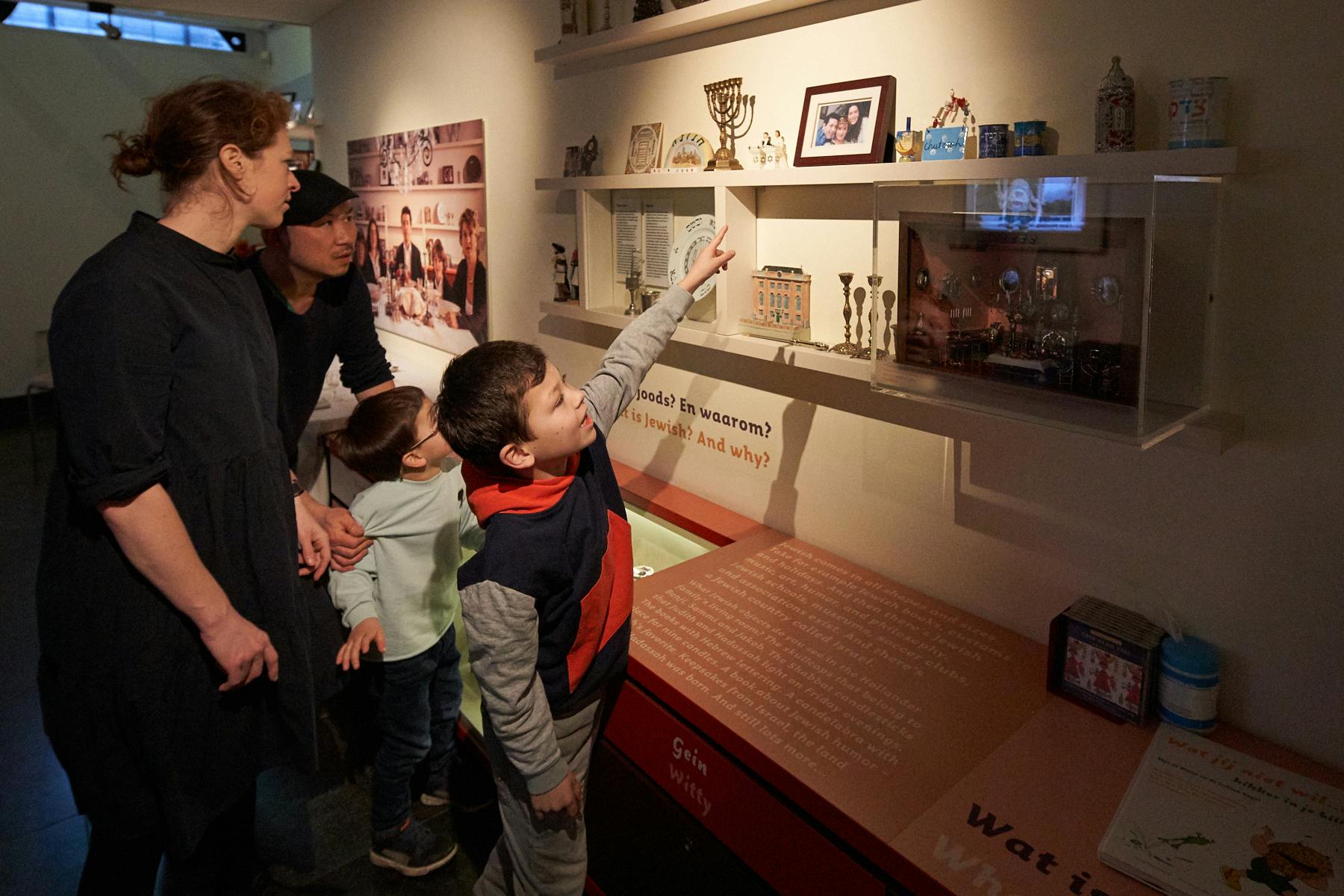 Deux adultes et deux enfants dans un musée regardant une vitrine avec divers objets et images sur le mur.