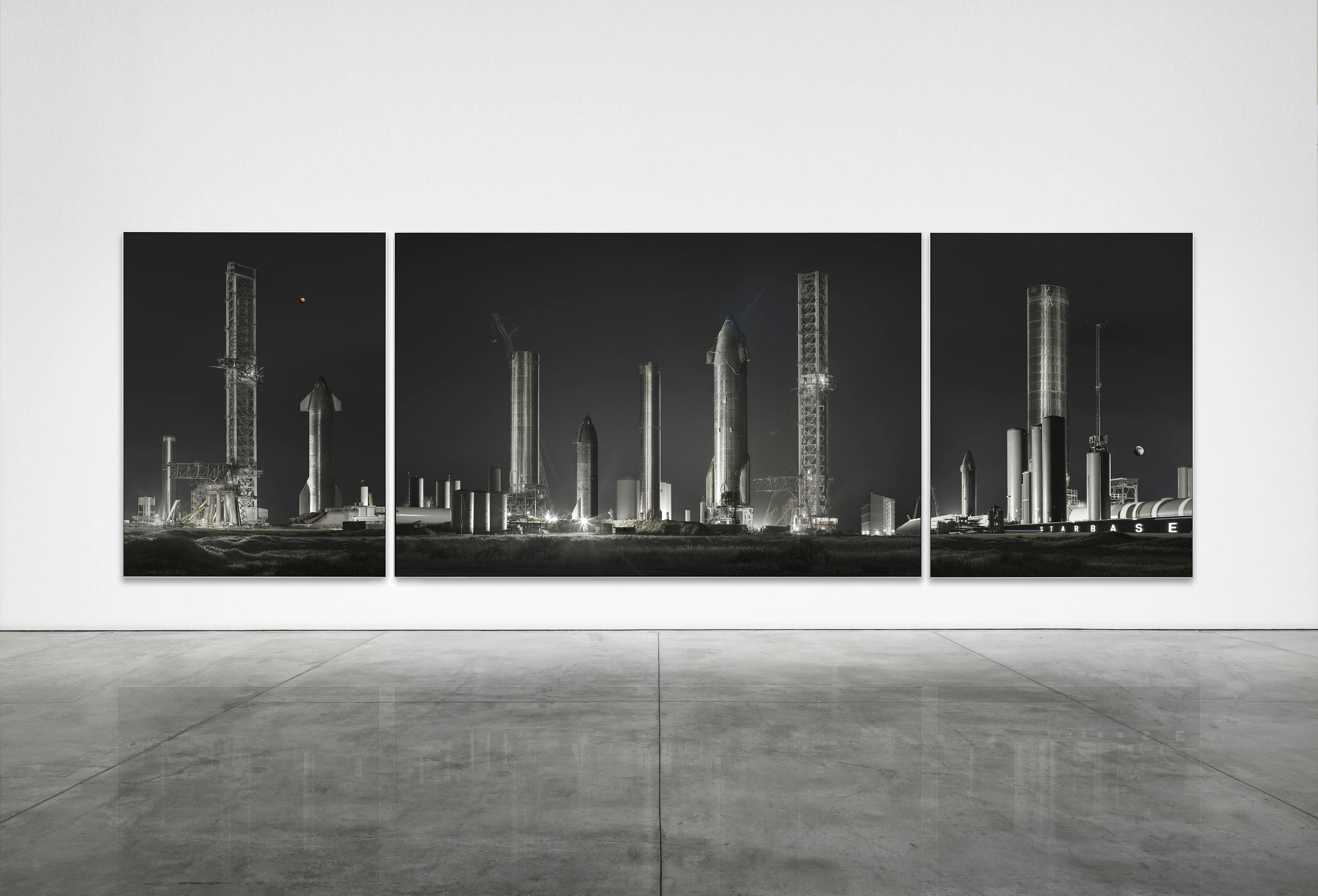 Una imatge de tríptic mostra diverses estructures de coets i torres de llançament contra un cel fosc i es mostra en una paret blanca.