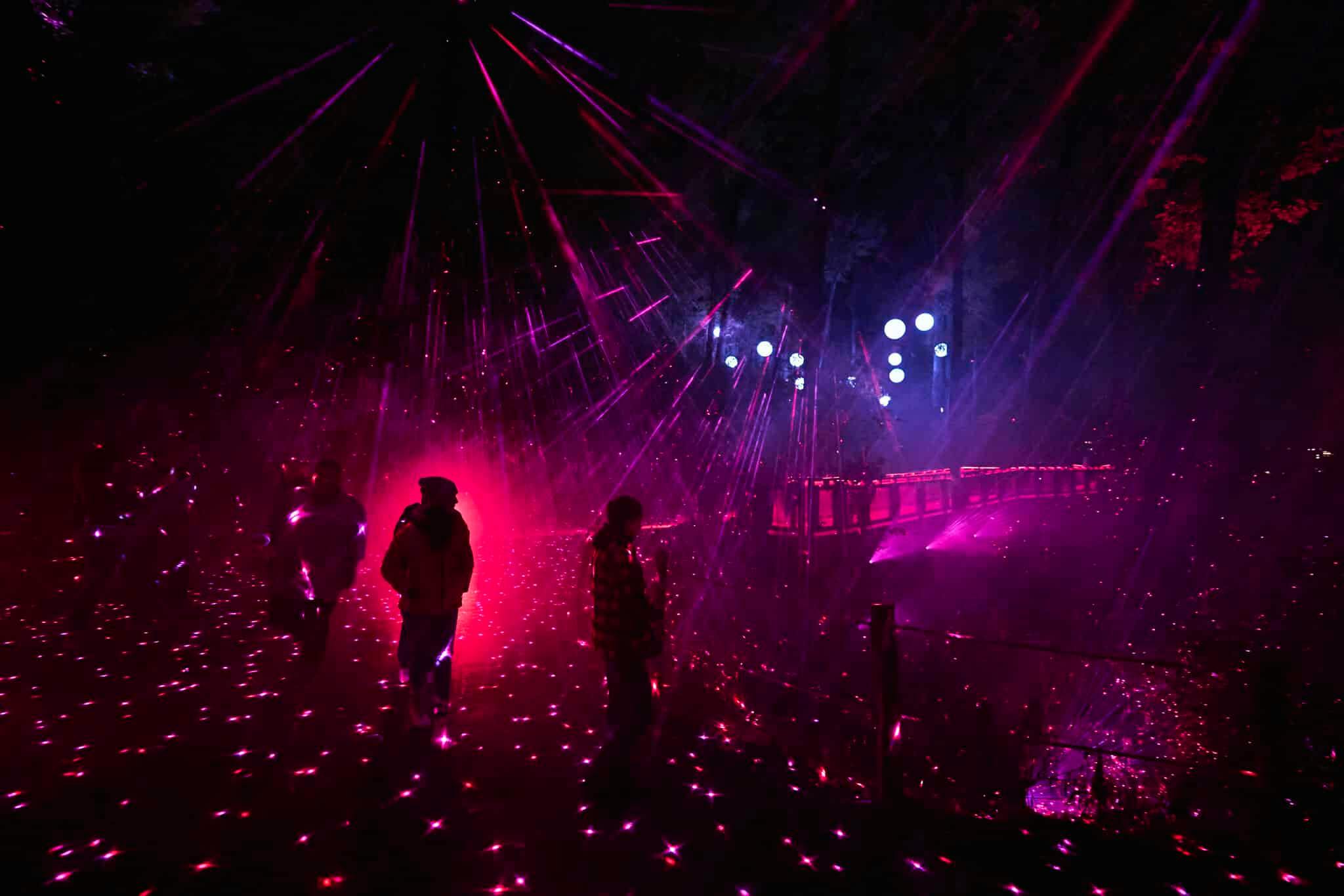 Люди, проходящие через темную область, освещенную красными и фиолетовыми огнями и лазерными лучами, создают яркую атмосферу.