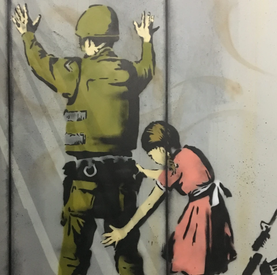Graffiti of a soldier being frisked by a young girl. The soldier has his hands up, and the girl wears a pink dress.