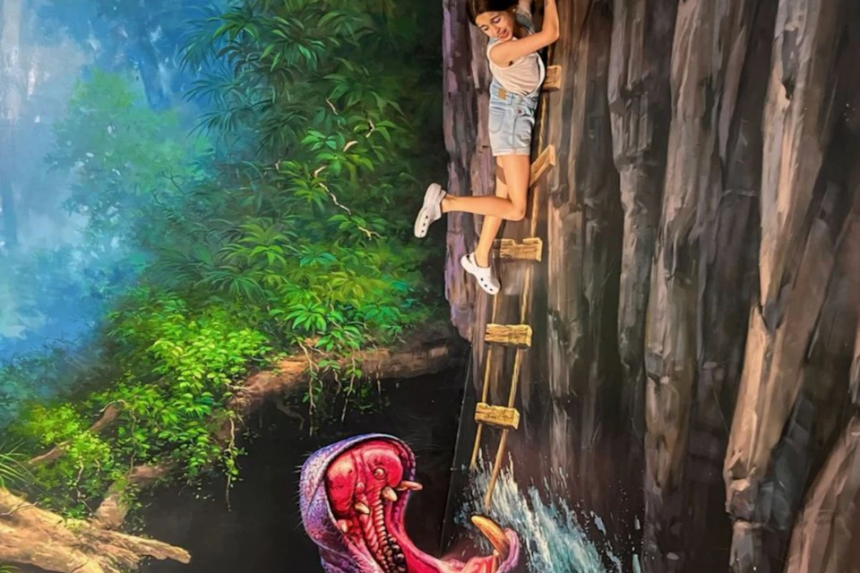 A person poses as if climbing a wooden ladder on a cliff, with a painted scene of a creature below and lush foliage in the background.
