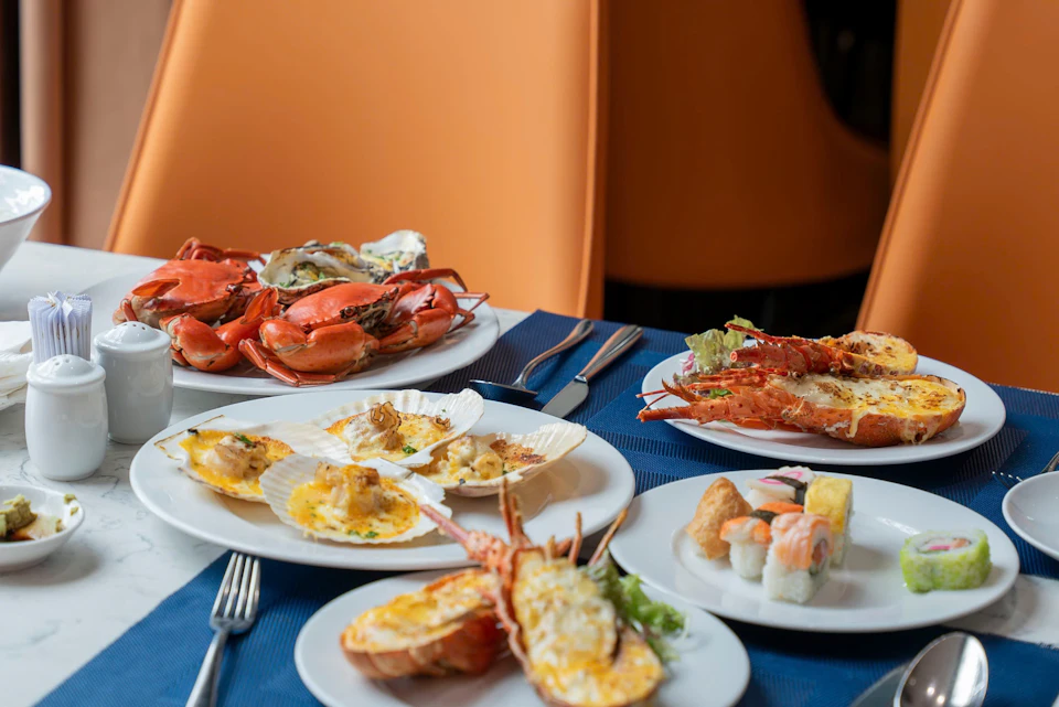 An assortment of seafood dishes, including crab, scallops, lobster, and sushi, served on white plates on a blue tablecloth.