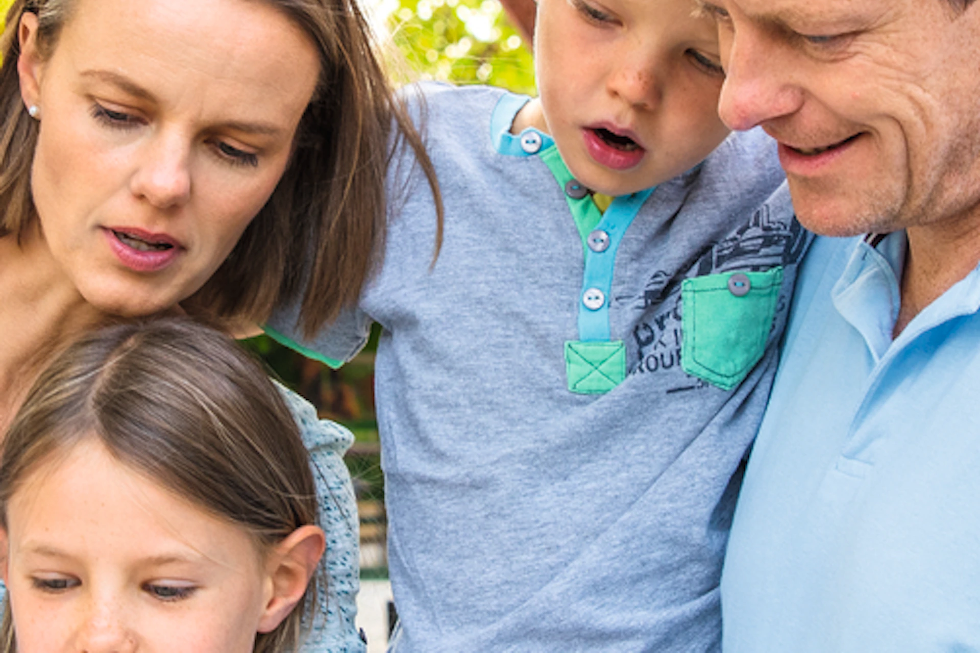 A family of four studies a map in front of the entrance to a zoo on a cobblestone path, with an archway labeled "Zoolog. Garten."