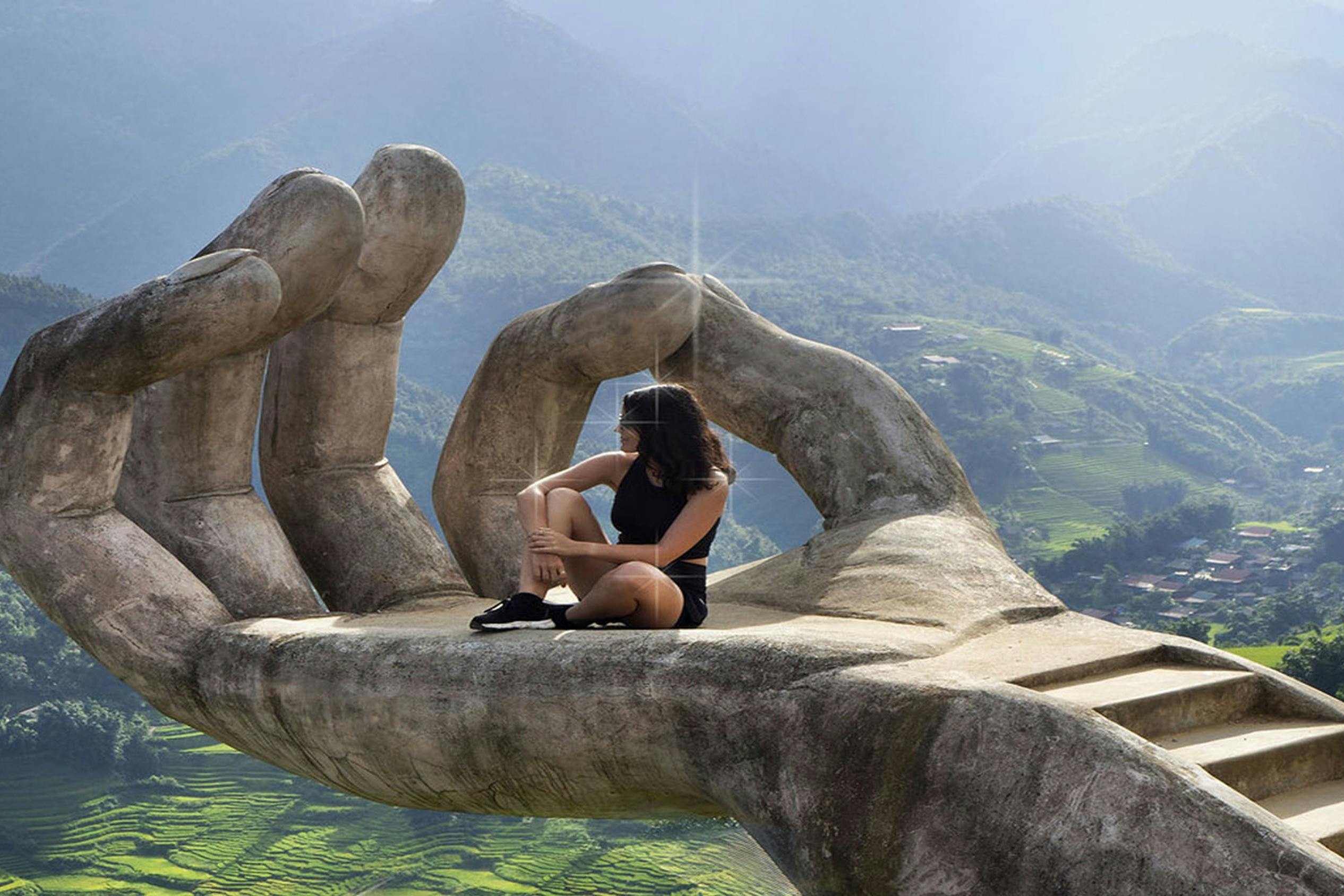 緑豊かな山の風景を見下ろす大きな石の手彫刻の上に人が座っています。