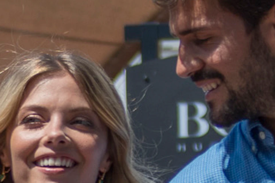 A smiling couple walks arm-in-arm along an outdoor shopping area, carrying shopping bags and enjoying a sunny day.