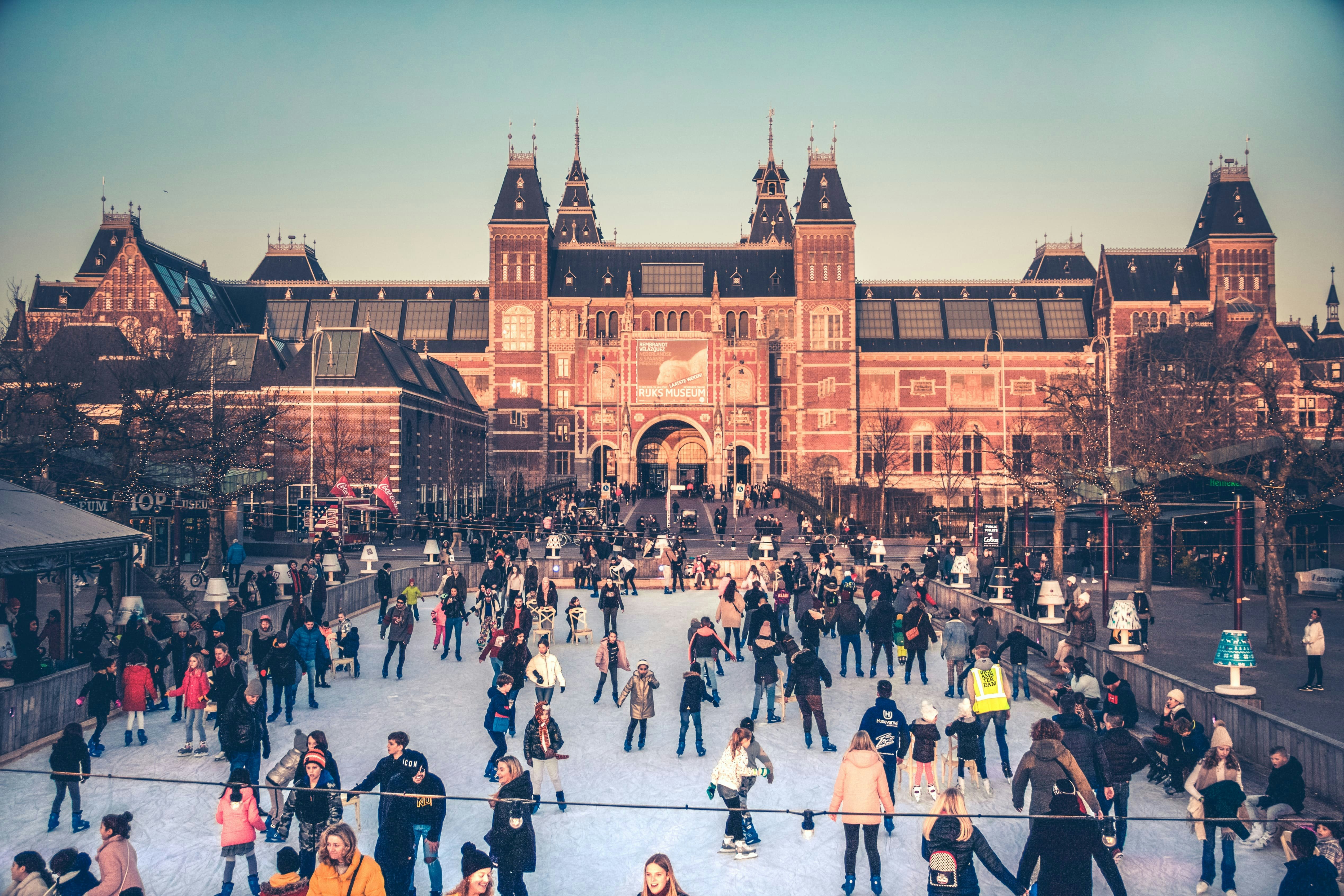 Mensen schaatsen op een ijsbaan met een groot, historisch gebouw op de achtergrond bij zonsondergang.