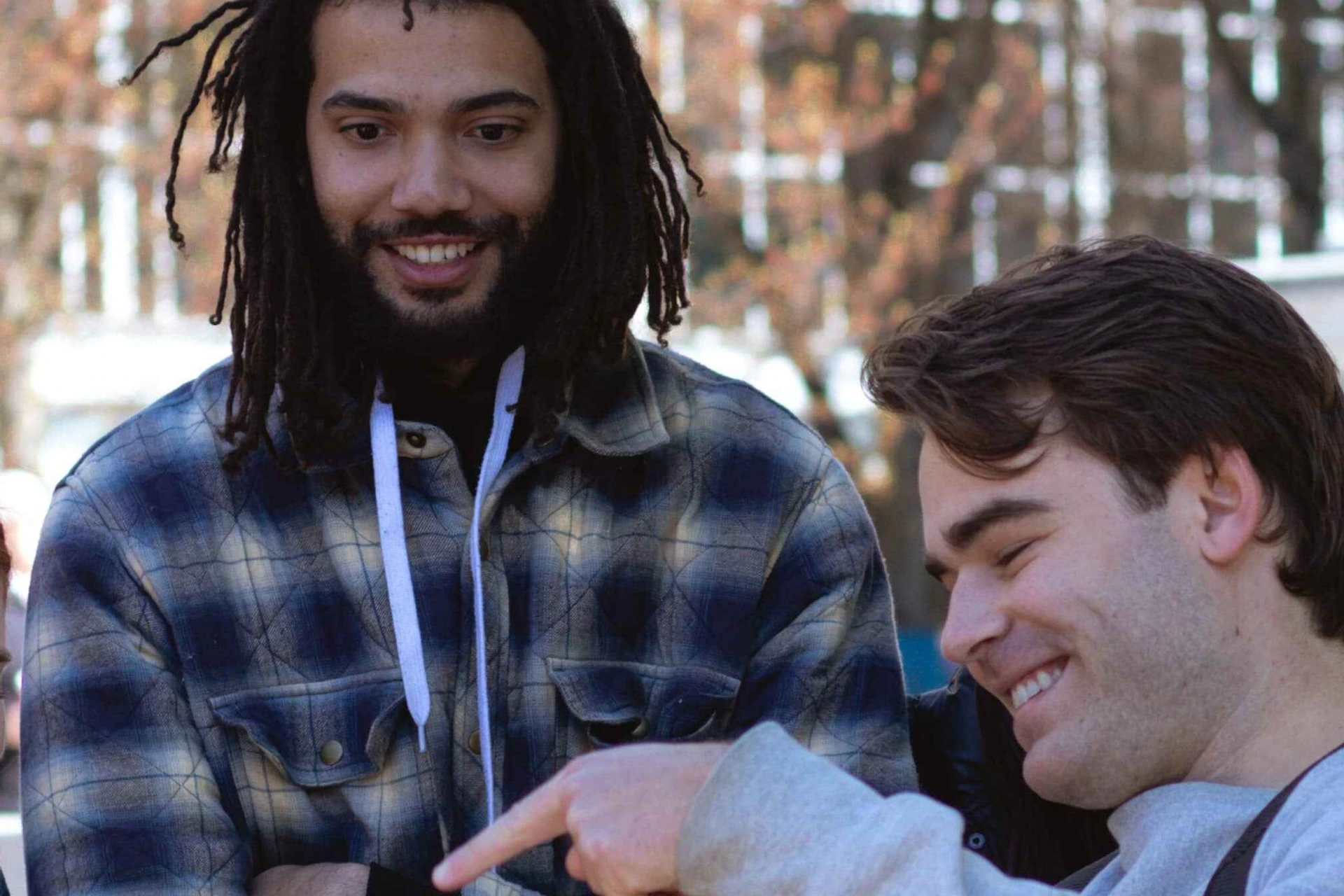A group of people outdoors looking at a tablet, with some smiling and one person pointing at the screen.
