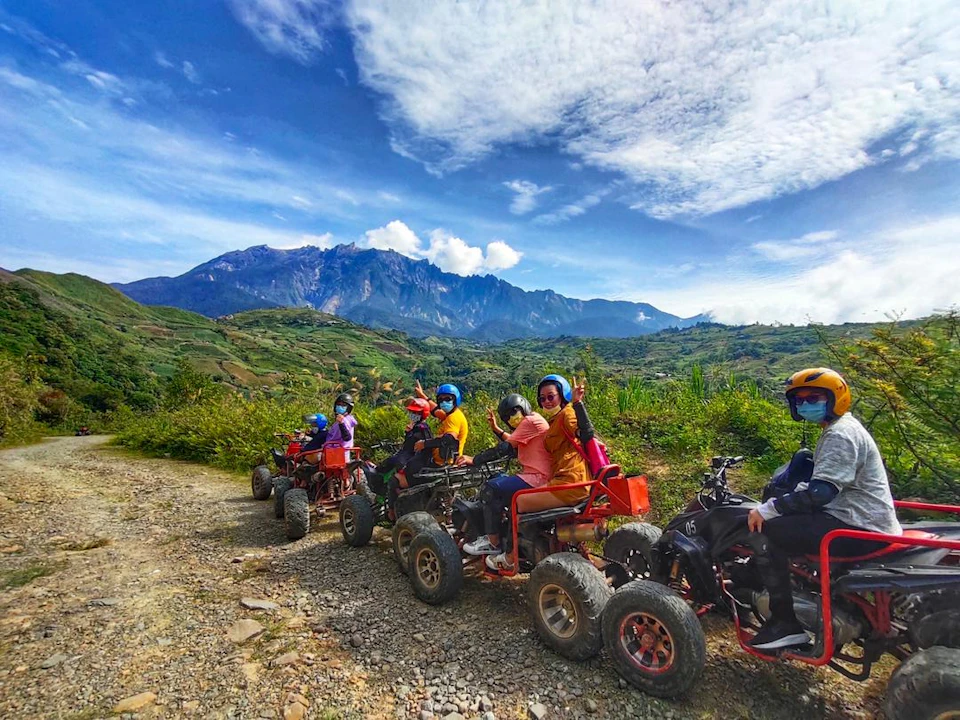A group of people riding all-terrain vehicles on a dirt path in a scenic mountainous area under a blue sky.