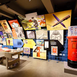 En museiutställning med historiska affischer, en röd stolpepostlåda, montrar med dokument och olika väggmonterade utställningar.