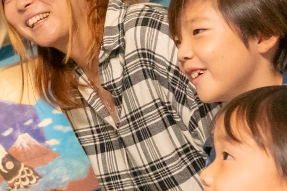 A woman and two children admire a colorful monster sculpture in a gallery with vibrant artwork on the walls.