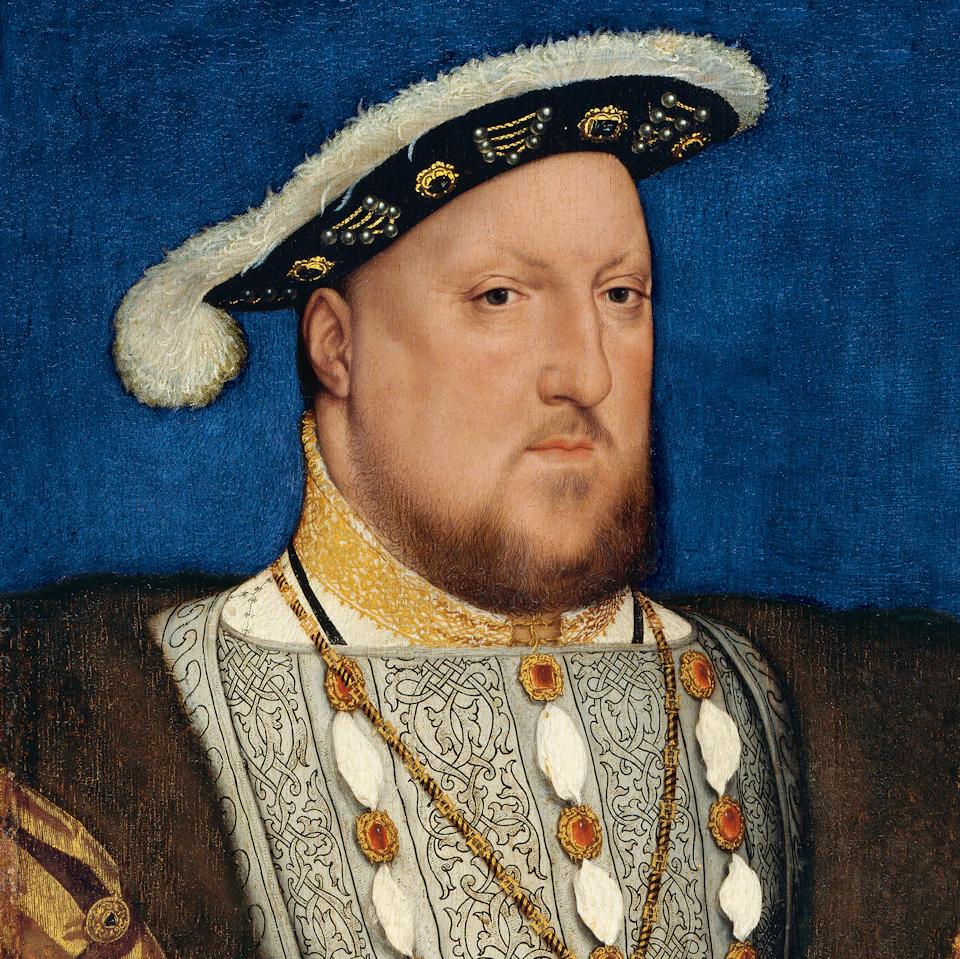 A man in regal attire with a beard and flat hat adorned with gold designs, set against a blue background.