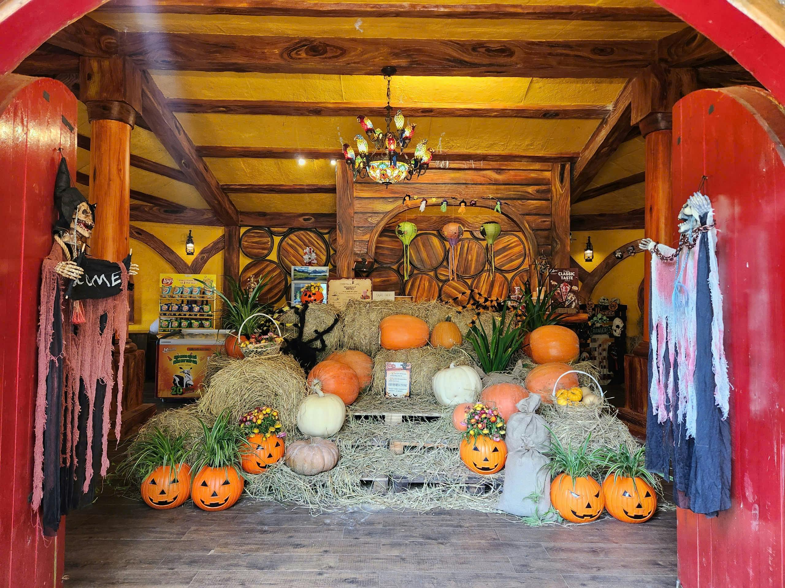 A festive autumn display with pumpkins, hay bales, and Halloween decorations in a rustic wooden interior.