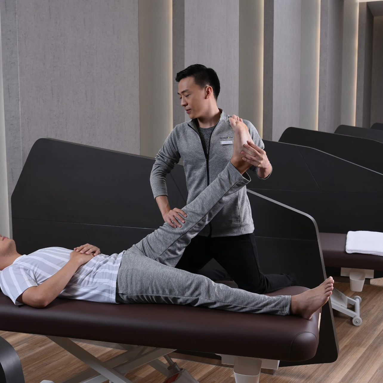 A therapist assists a patient with a leg stretch on a treatment table in a modern therapy clinic.