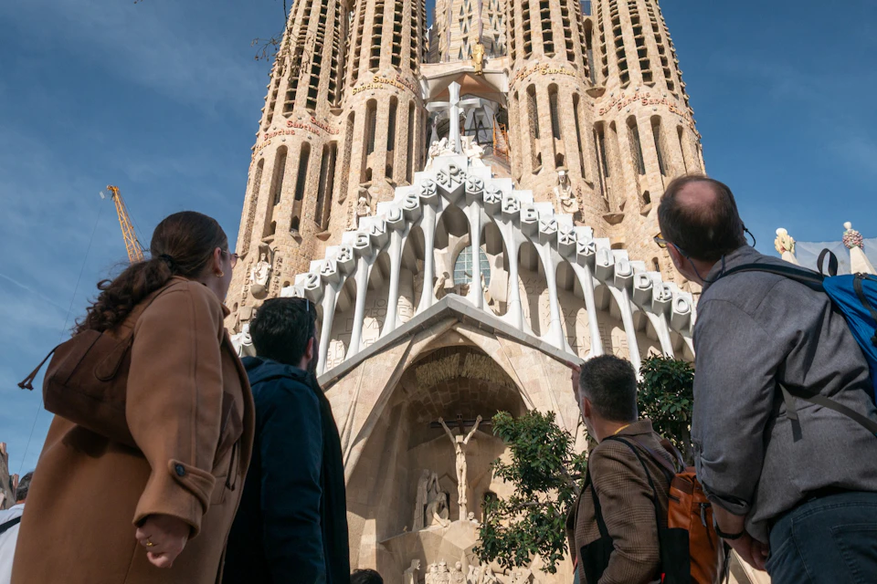 A group of people standing in front of the Sagrada Família basilica, admiring its intricate facade and tall towers.