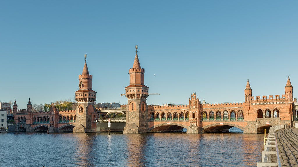 A red brick bridge with two towers spans across a river under a clear blue sky.