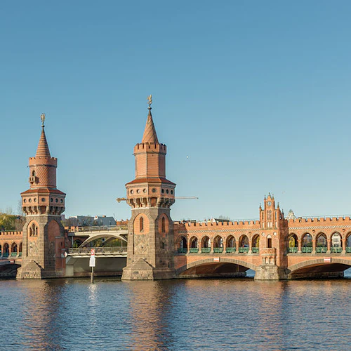 En röd tegelbro med två torn sträcker sig över en flod under en klarblå himmel.