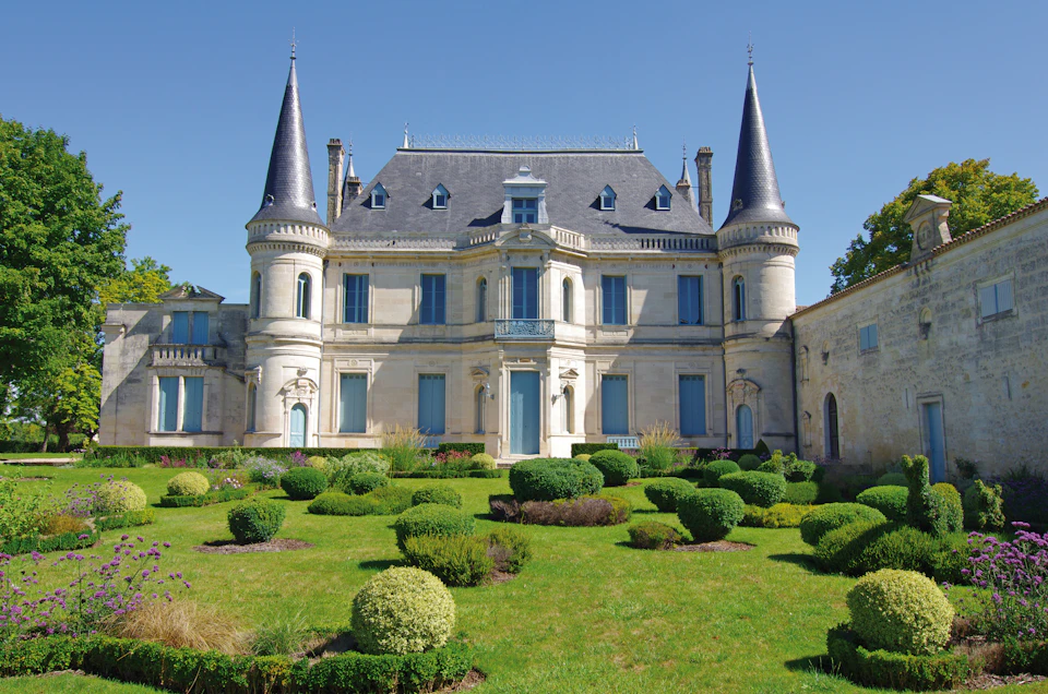 A large, elegant château with conical towers and manicured gardens beneath a clear blue sky.