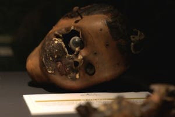 Ett skadat dockhuvud med saknade delar som visas på en yta, med ett dokument som är delvis synligt under det.