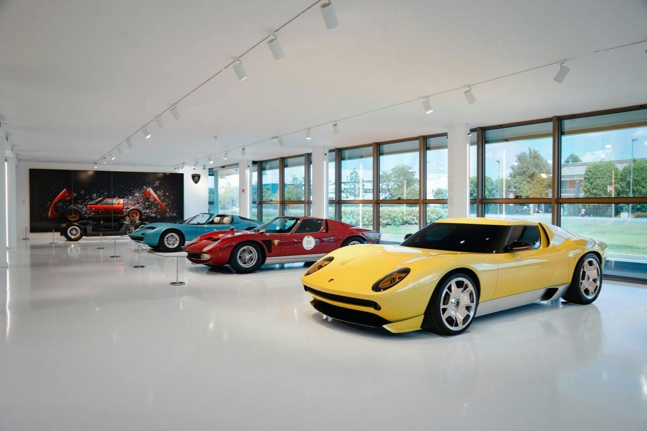 Et moderne showroom, der viser en samling af klassiske biler og konceptbiler, herunder en gul sportsvogn i forgrunden.