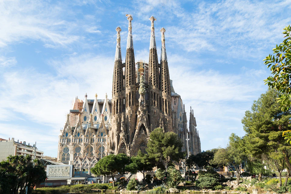 A large and ornate cathedral with tall spires under a blue sky, surrounded by trees and greenery.