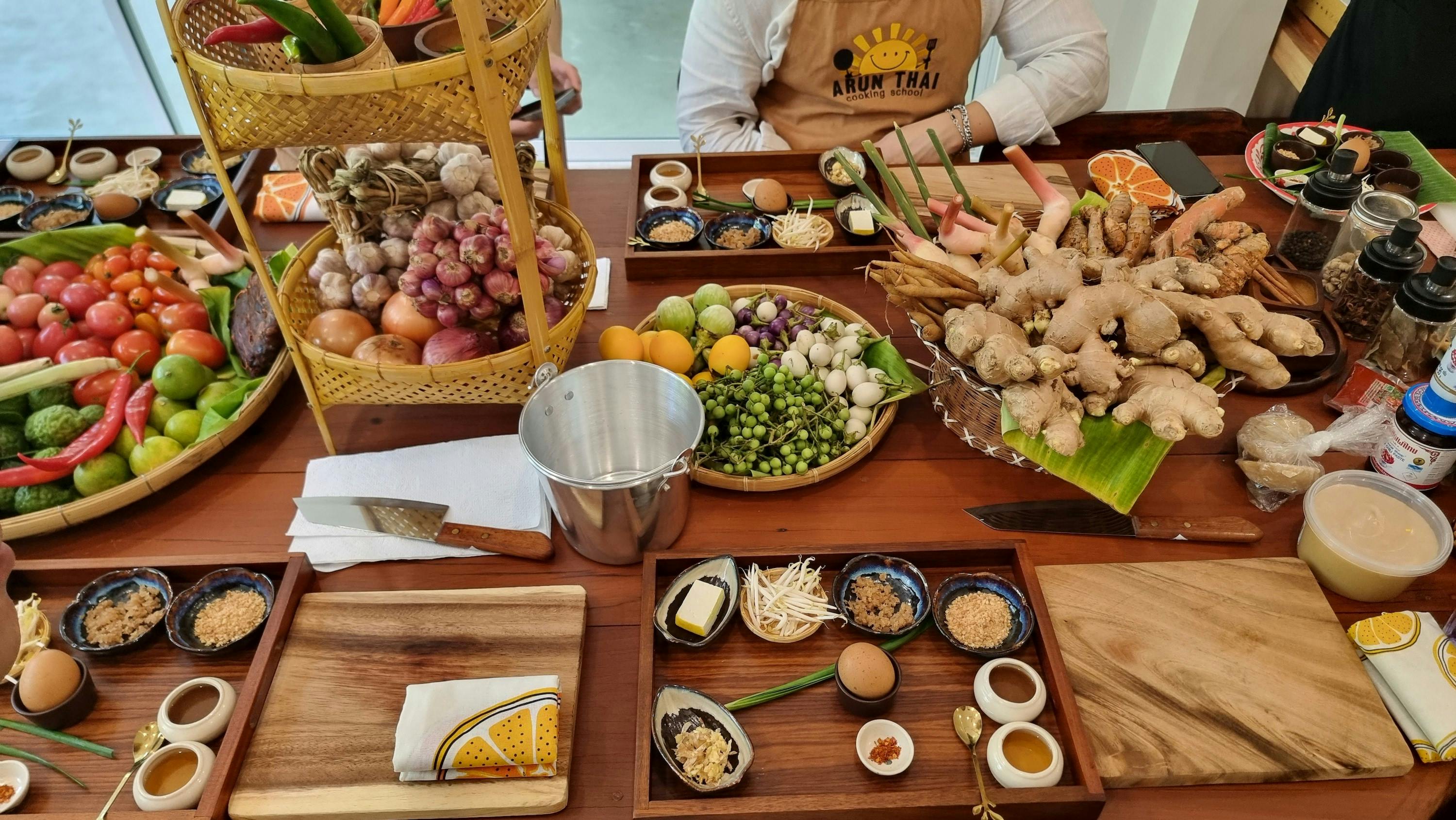 A cooking class setup with ingredients like herbs, vegetables, and spices on a table. A person wearing an apron is visible.