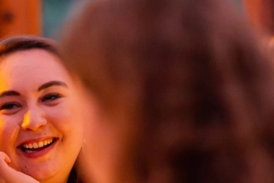 A group of people seated at a table in a warmly lit setting, engaging in conversation and smiling.