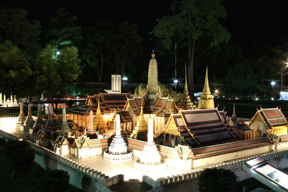 An intricately lit miniature model of a temple complex at night, surrounded by trees and illuminated by spotlights.