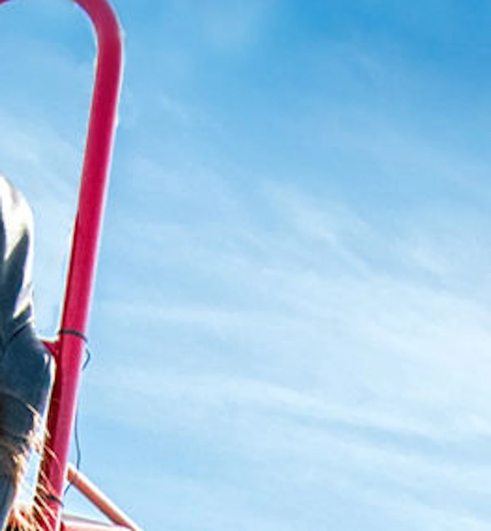 Three people riding red go-karts on a track, smiling and looking excited under a blue sky.