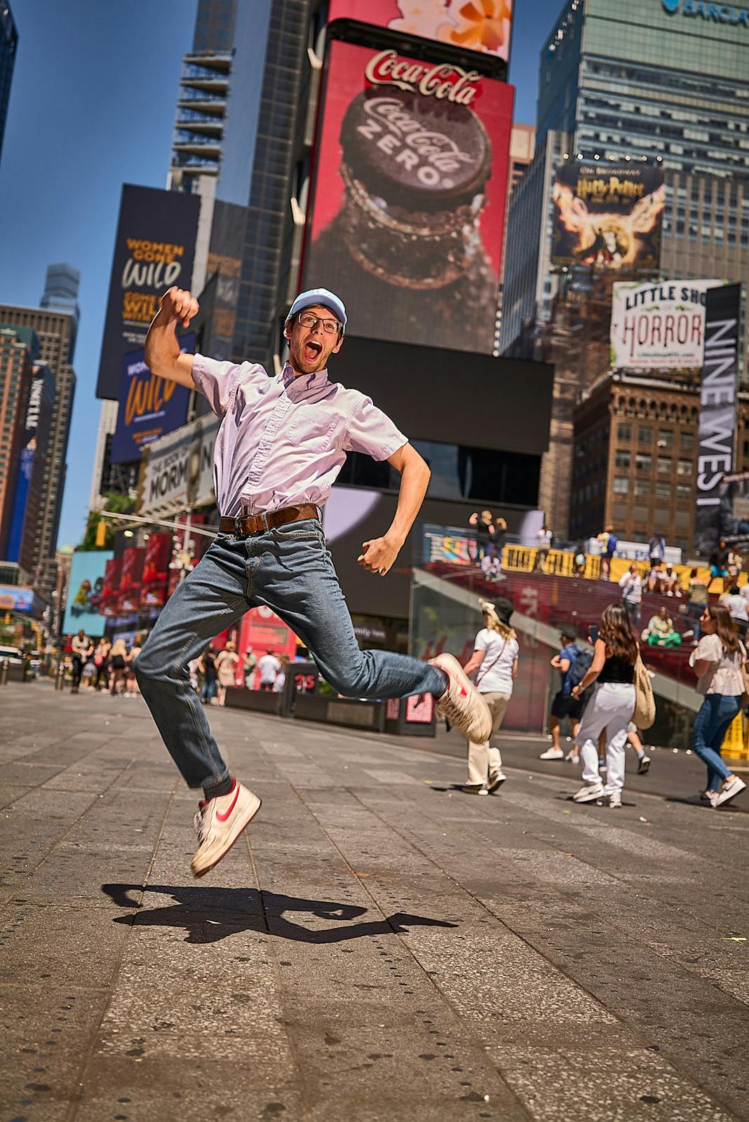 Άτομο που πηδάει χαρούμενα στην Times Square της Νέας Υόρκης, περιτριγυρισμένο από ψηλά κτίρια και φωτεινές διαφημιστικές πινακίδες.