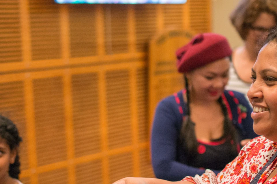 A woman hands a certificate to a young person while others stand in the background, smiling indoors.