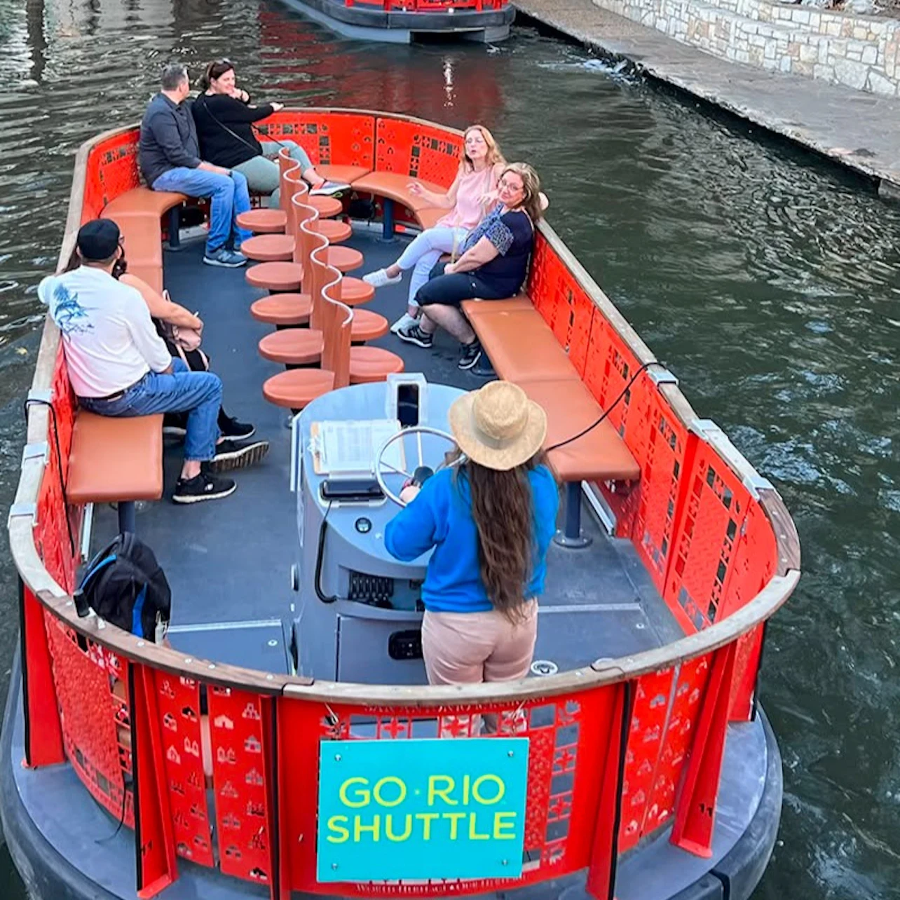 A river shuttle boat with passengers seated along the sides and a guide steering at the front, labeled 'GO RIO SHUTTLE.'