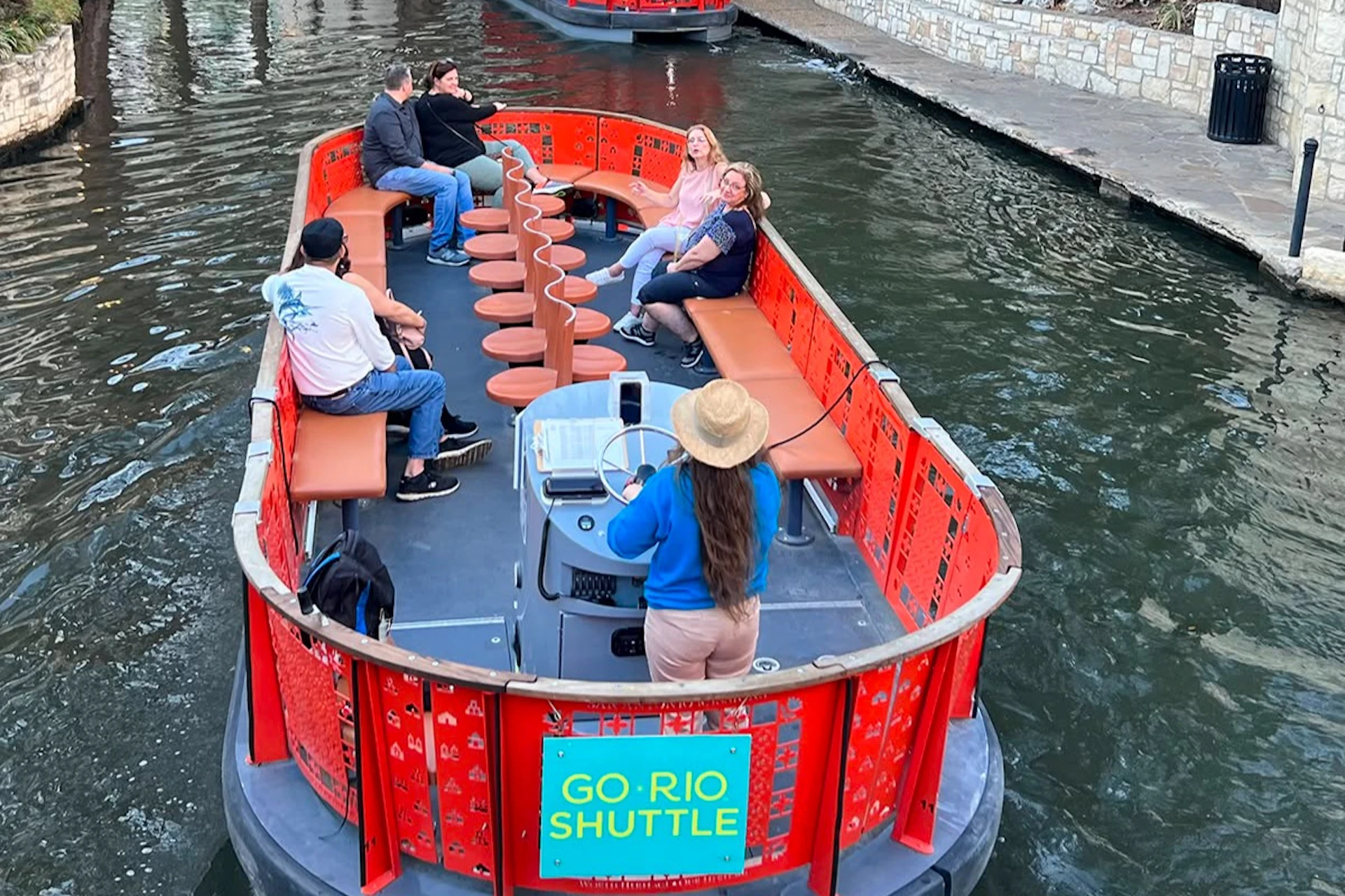 A river shuttle boat with passengers seated along the sides and a guide steering at the front, labeled 'GO RIO SHUTTLE.'