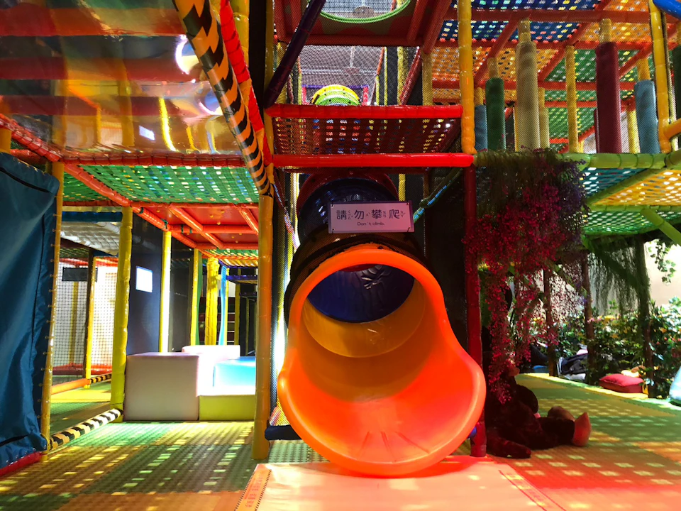 A colorful indoor playground with a slide tube entrance, climbing structures, and play areas under vibrant lighting.