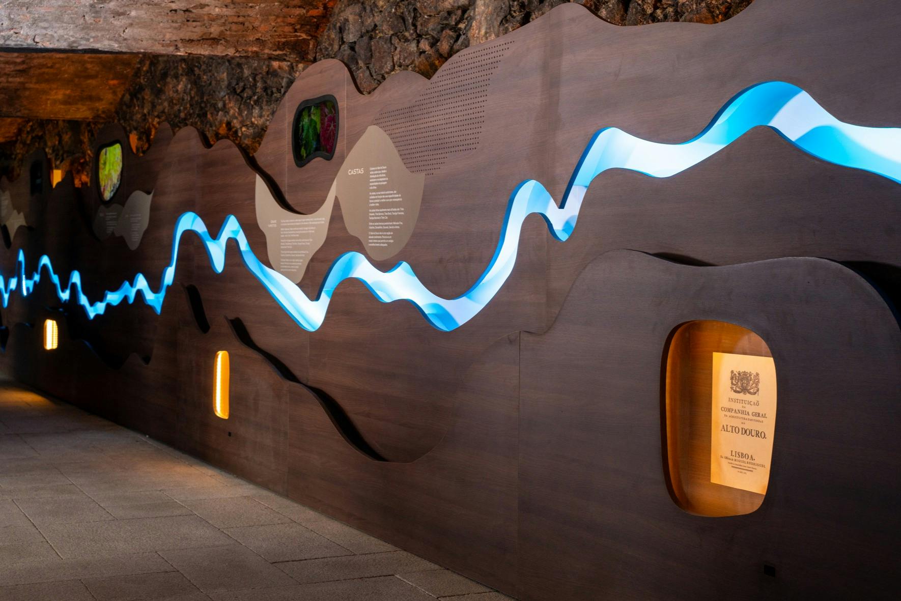 Installation murale présentant des contours ondulés avec un éclairage bleu, des plaques d'information et des panneaux d'affichage encastrés.