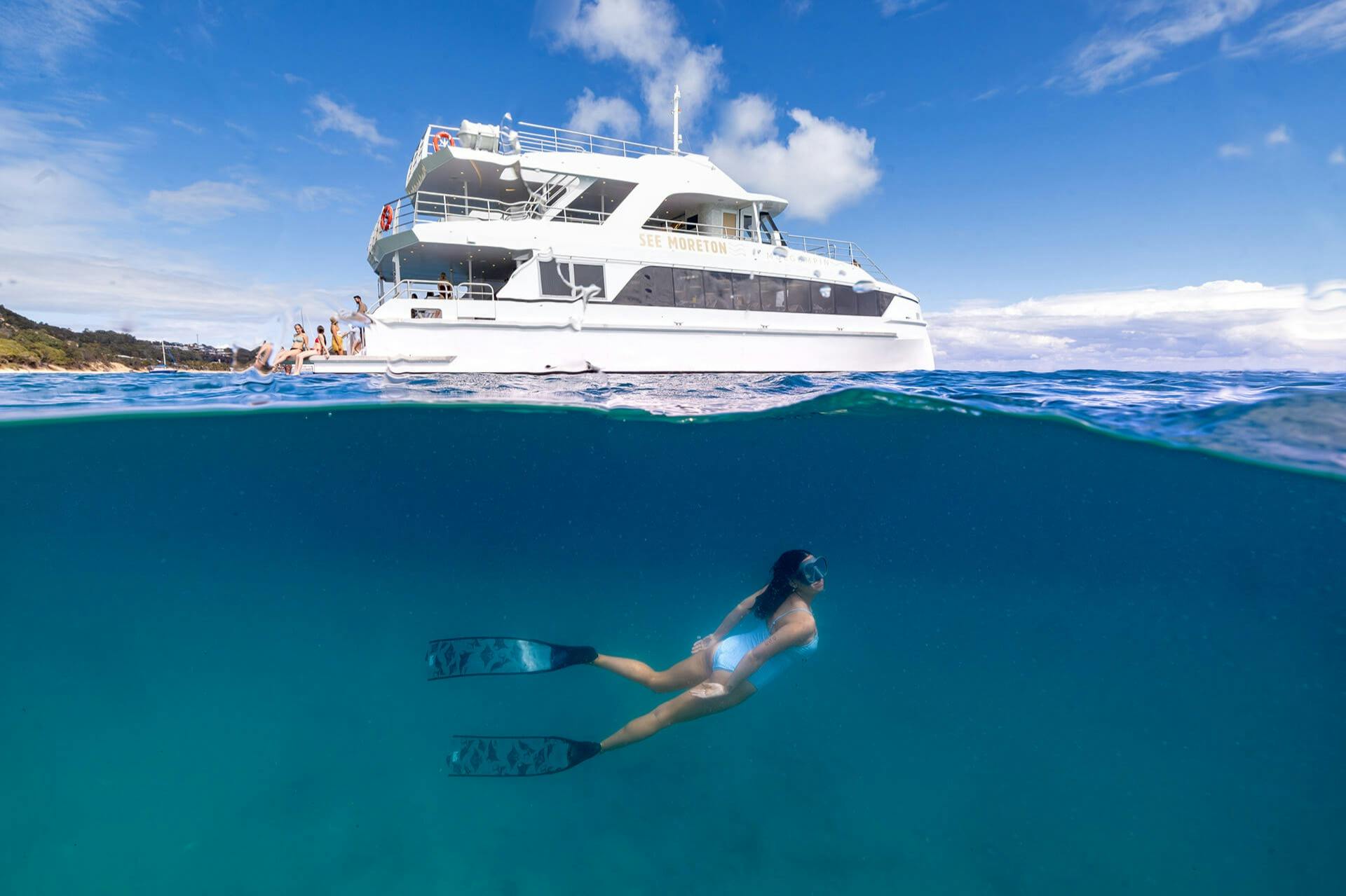 Een grote boot op het oceaanoppervlak met mensen aan boord en een snorkelaar onder water met vinnen, in een split-view perspectief.