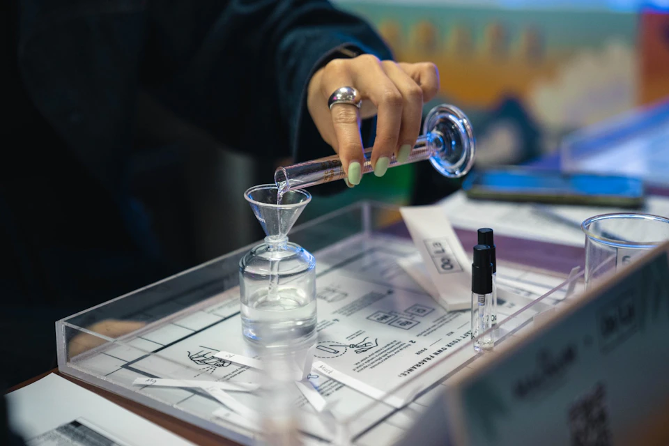 A person pouring liquid into a glass funnel over a container, with small bottles and paper notes on a tray nearby.