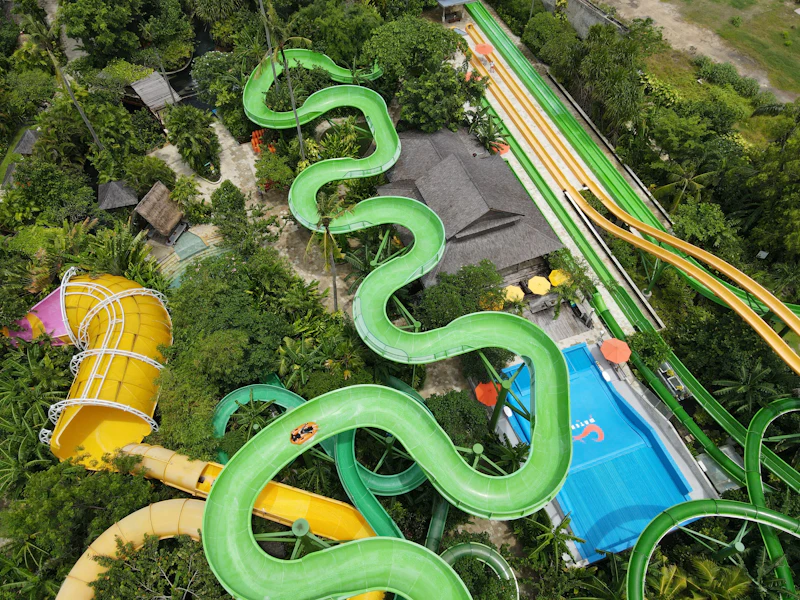Aerial view of a water park with winding green slides, a pool, and surrounding greenery and structures.