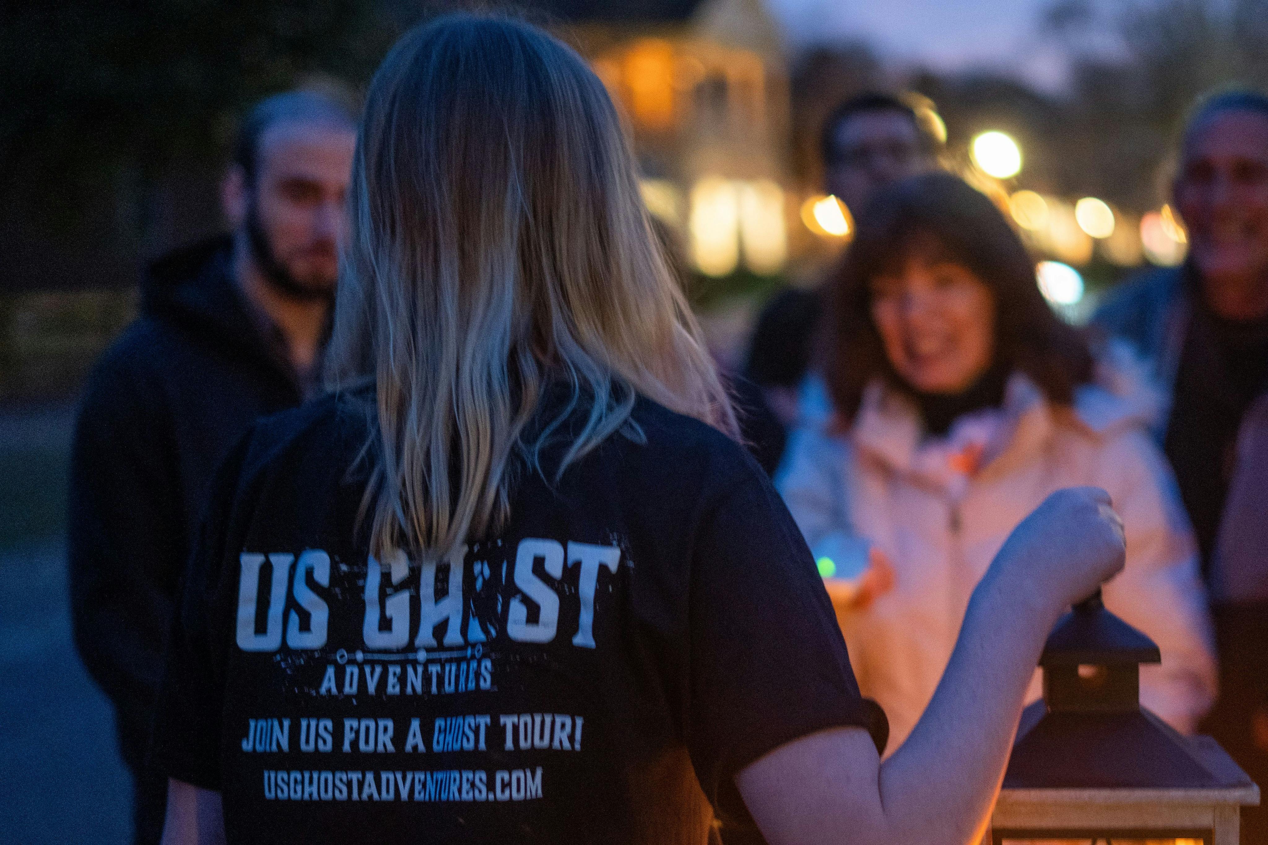 Tour guide holding a lantern as guests surround her to listen to ghost stories