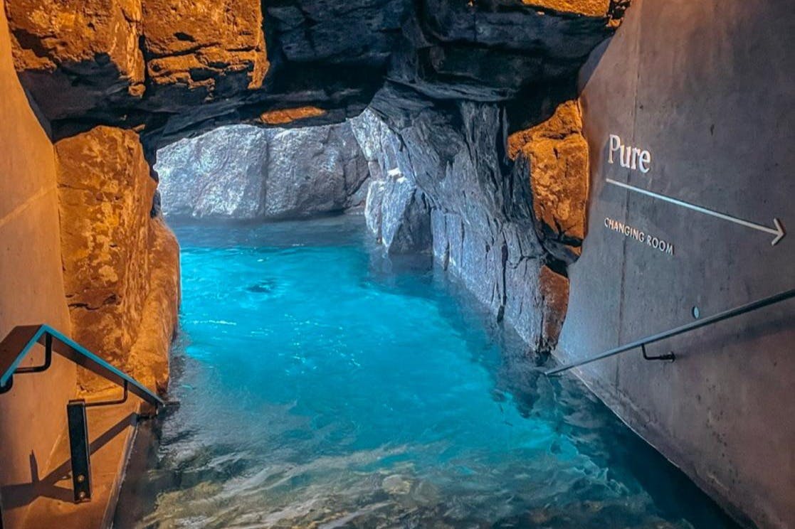 Průzračný modrý bazén uvnitř skalnaté jeskyně s cedulemi pro šatnu na pravé stěně.