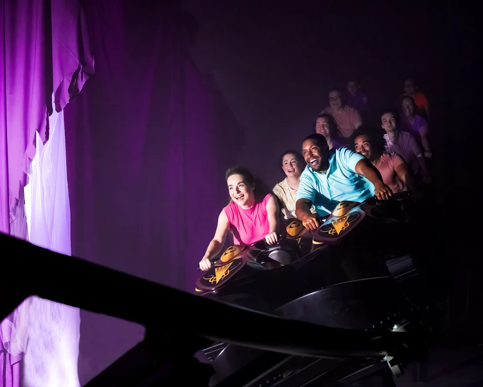 People smiling and laughing as they ride a roller coaster in a dimly lit environment.