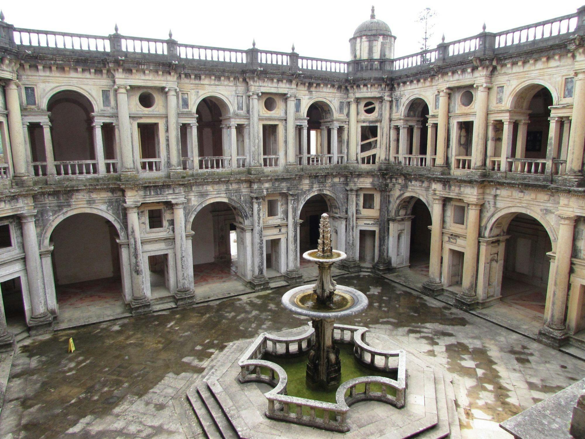 中央には華やかな階層の噴水があり、アーチ型の窓と出入り口がある2階建ての建物に囲まれた古い石造りの中庭。