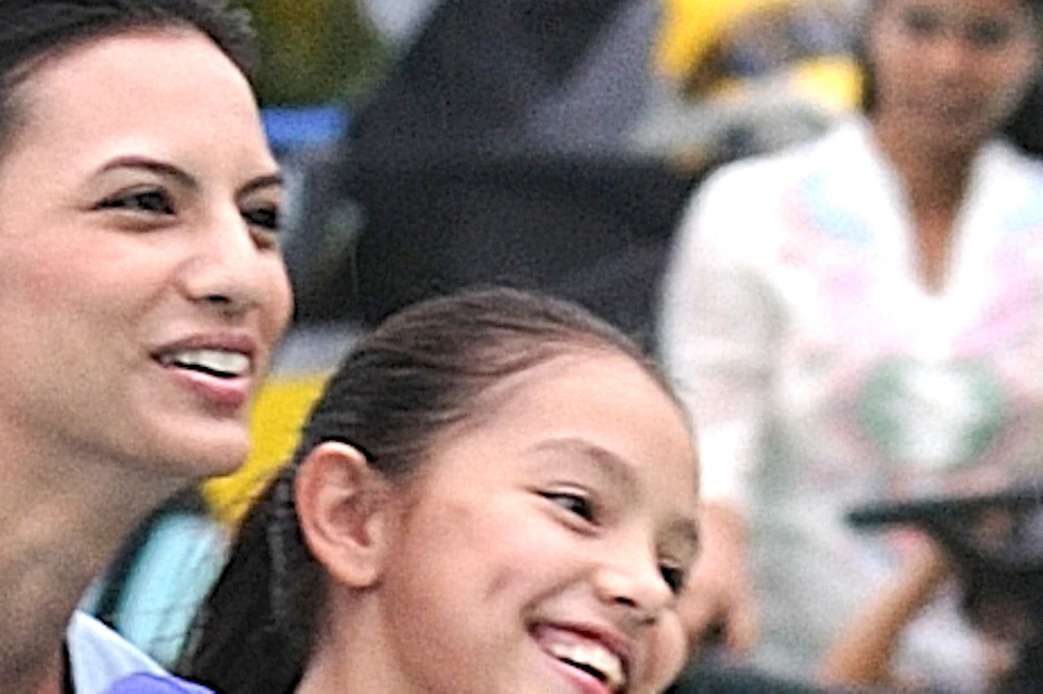 Two people smiling while riding a yellow water ride, with a blue structure and lush greenery in the background.