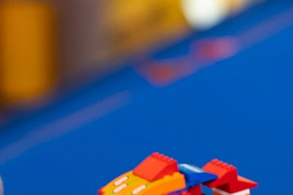 Two children at a table playing with colorful LEGO bricks, one holding a LEGO car, with a blurred background.