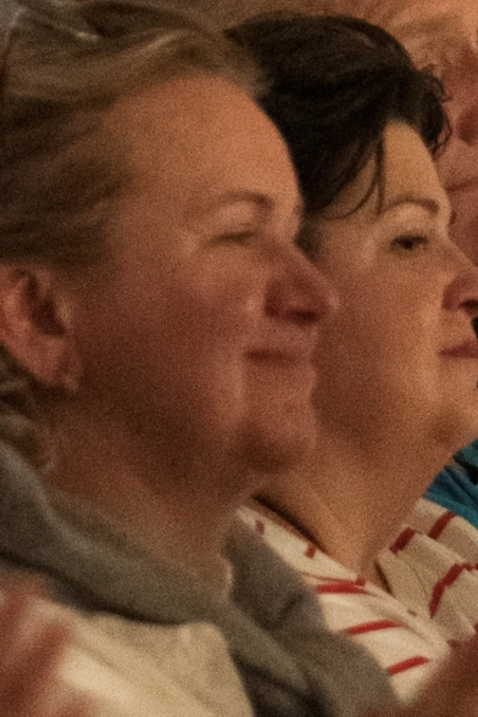Audience members seated and applauding in an ornately decorated room with a sign labeled "Schumann" on the wall.