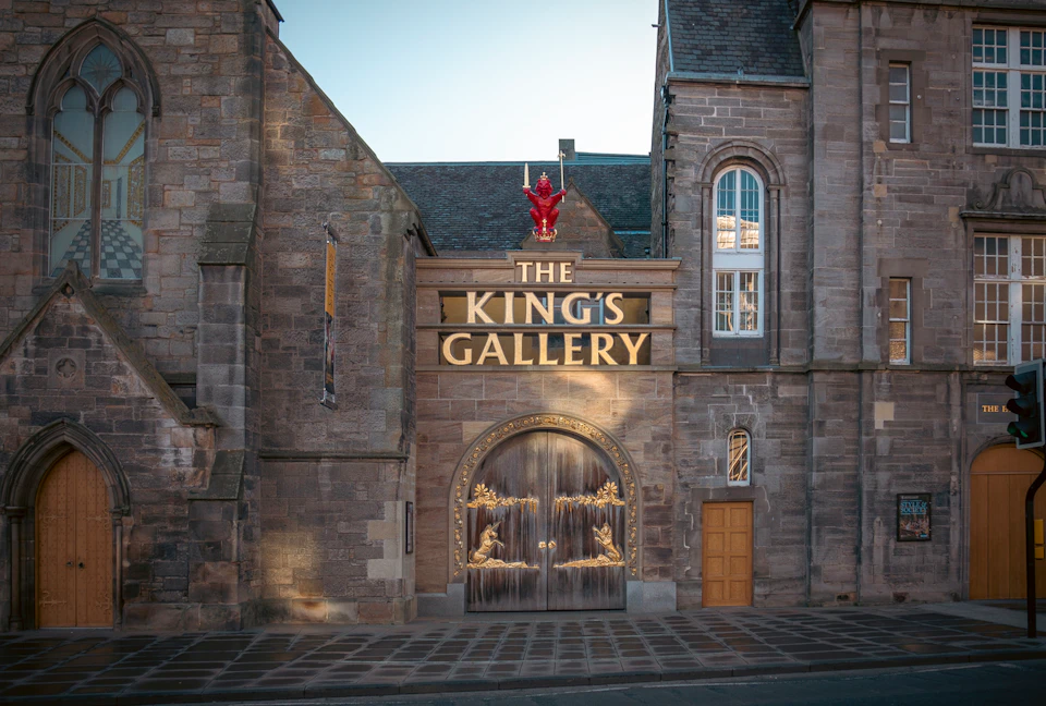 Stone building facade with an arched doorway, ornate carvings, and a golden "THE KING'S GALLERY" sign above.