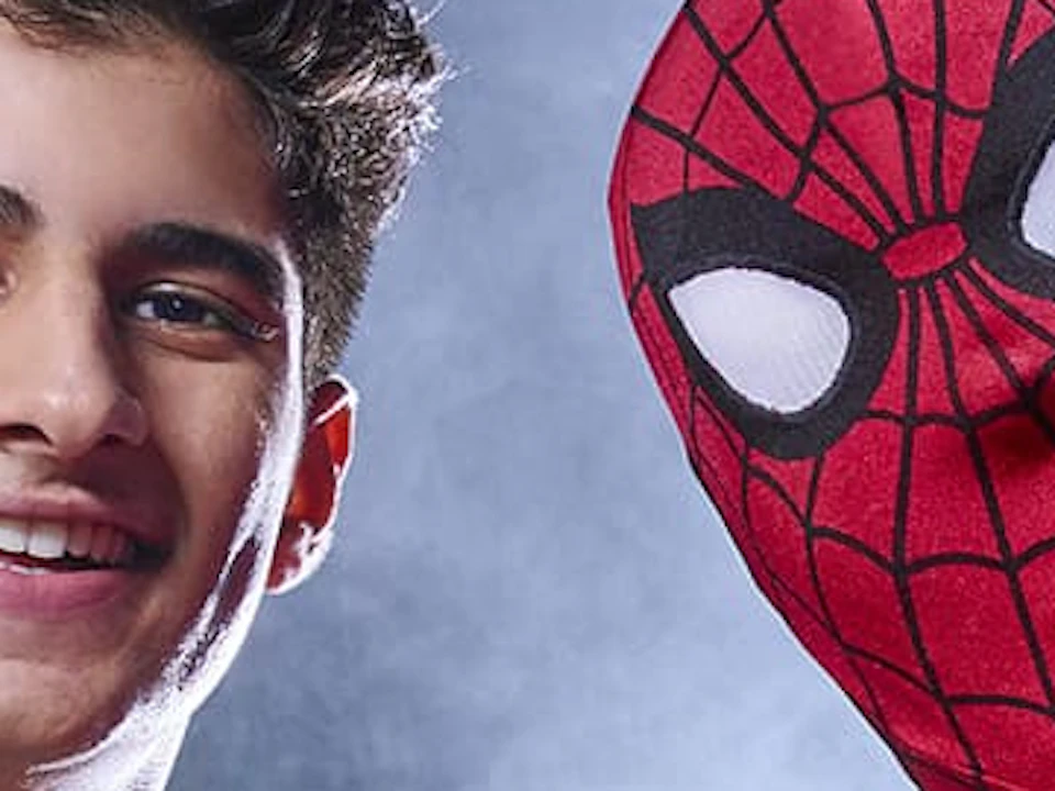 A person in a white sweater poses with someone in a Spider-Man costume in a cityscape with a Spider-Man sign in the background.