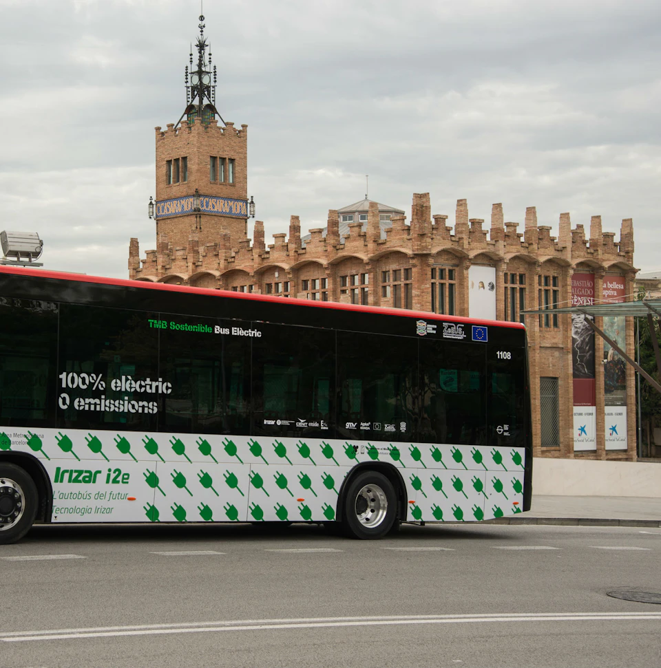 An electric bus displaying "100% electric, 0 emissions" is parked on a street with a historic, ornate building in the background.