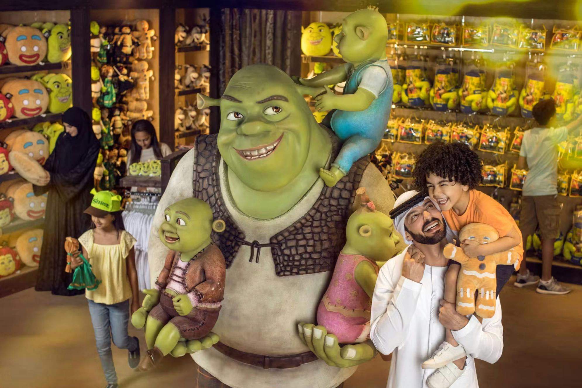 A Shrek statue holding three children dolls in a toy store. Customers browse in the background.