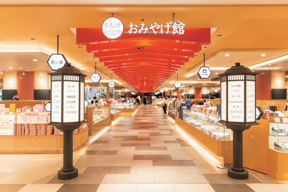 A brightly lit shopping arcade with red ceiling panels, signage, and display cases along both sides.